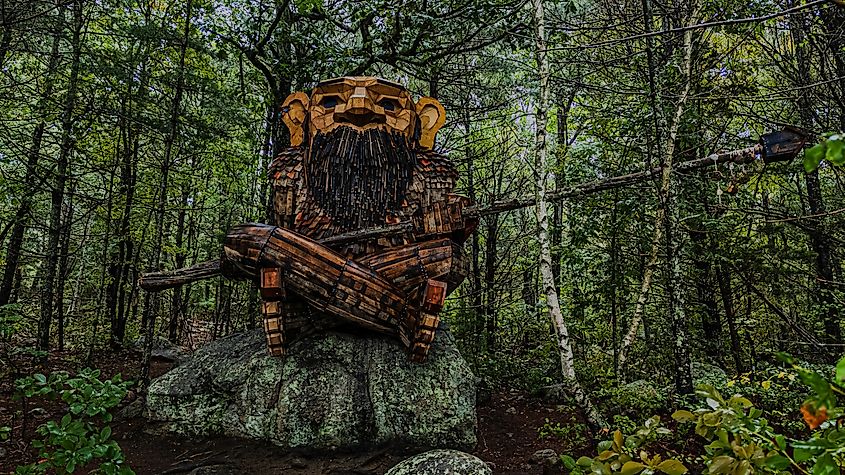 Editorial Photo Credit: Audley C Bullock via Shutterstock. Arcadia Management Area, RI USA - September 7, 2025: A high angle view of Young Boulder, one of Thomas Dambo's wooden trolls in Rhode Island's Arcadia Management Area near Browning Mill Pond, cloudy. 