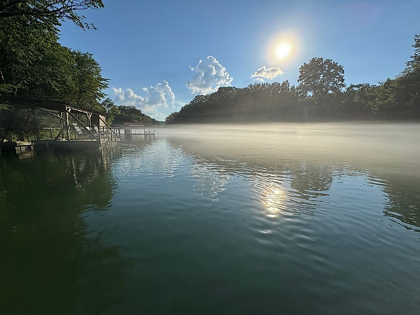 Peaceful reflection of sun, trees, clouds and docks on misty Little Red River Arkansas.