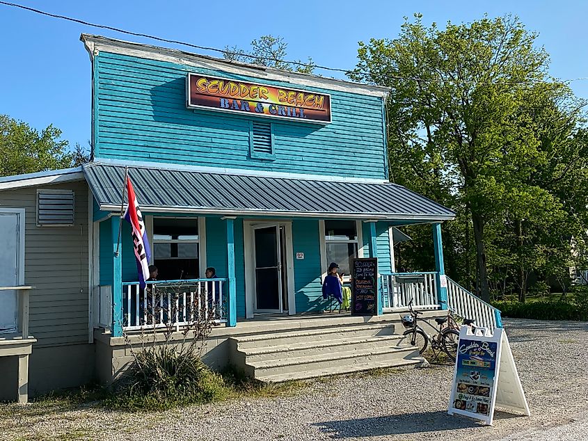 A blue restaurant with a picket fence patio called Scudder Beach Bar & Grill