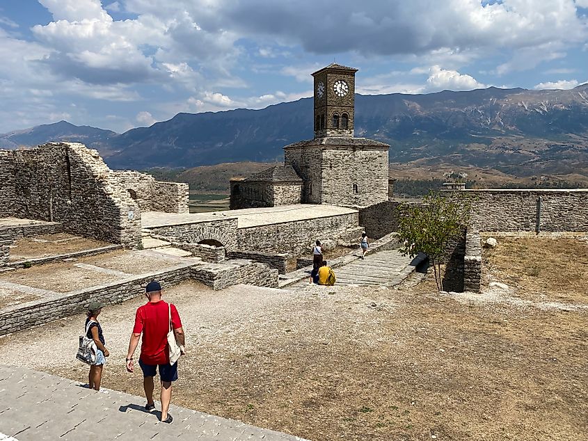 A yellow-grass courtyard with striking clock tower atop a castle in the Albanian mountains.