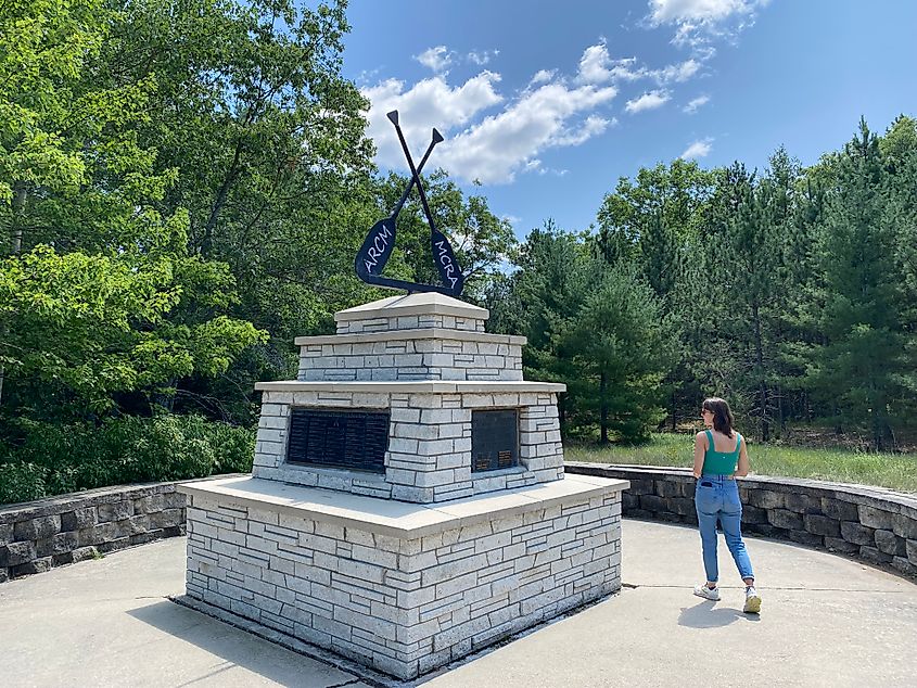 A woman walks around a stone monument with plaques and canoe paddles attached to it.