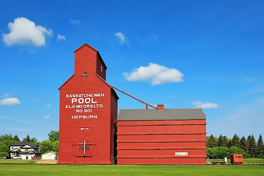 Old wooden grain elevator in Hepburn, Saskatchewan standing tall beside a grassy field under a partly cloudy sky