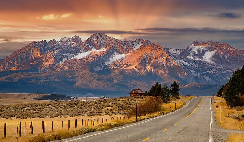 The Sawtooth mountains and a log cabin at sunrise and highway 75 leading to Stanley, Idaho.