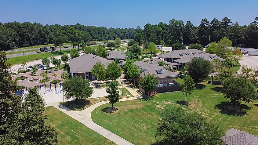 Aerial view of the pavilion and buildings with shingle roofs at the welcome center and rest area in Greenwood, Louisiana, along highway I-10. The scene includes a concrete pathway, well-trimmed yard, and outdoor post lights for car and truck stops.