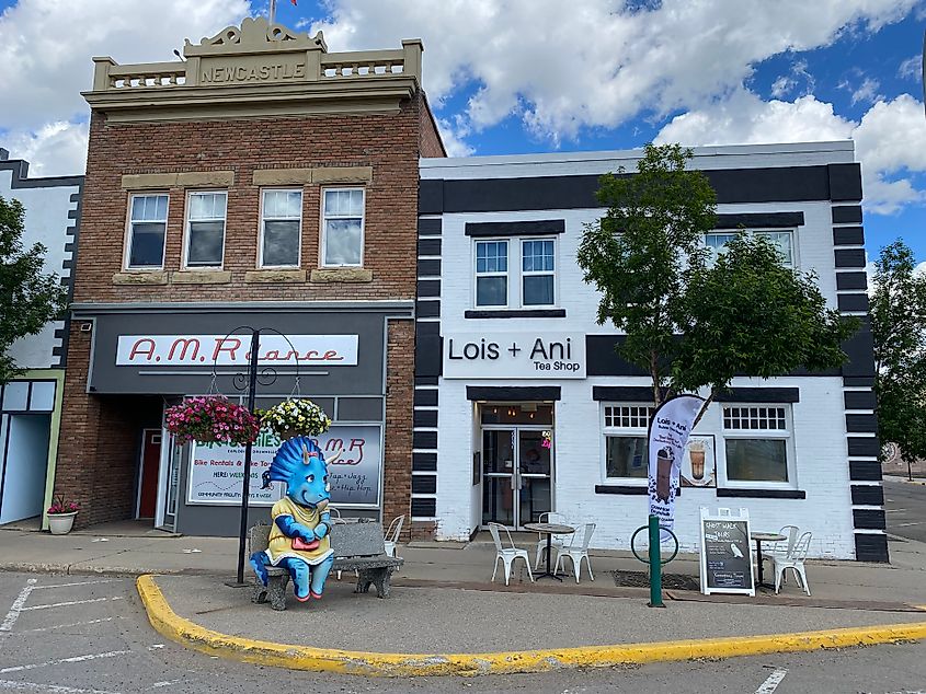 A cutesy, cartoonish triceratops statue sits on a bench outside of a couple of small boutique shops.