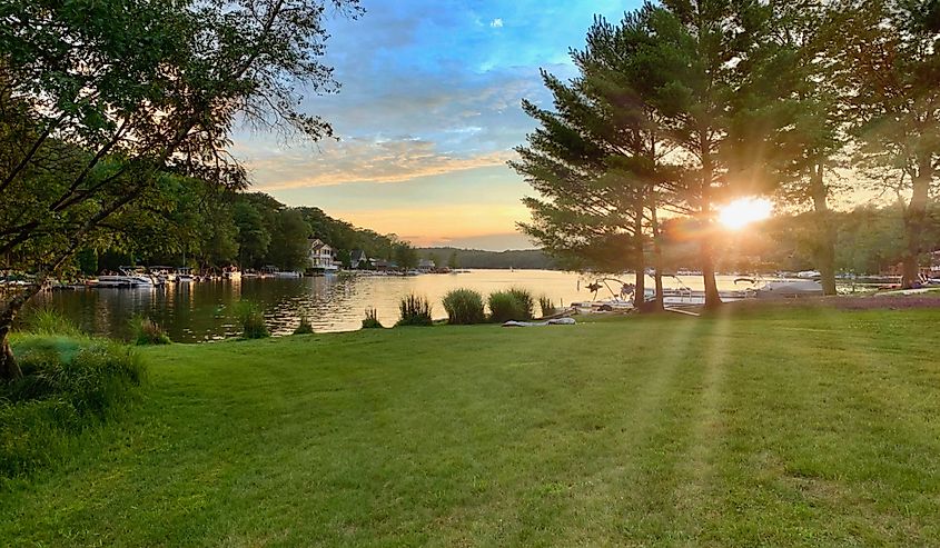 Sunset over Lake Harmony, sun peeking through the trees and reflecting off the water against a blue sky.