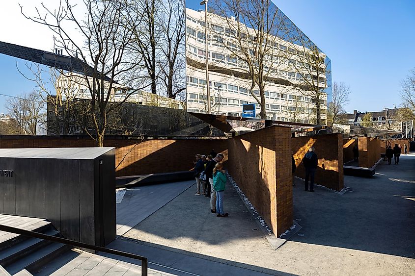 People visiting the Dutch National Holocaust Name Monument with brick walls and reflective mirroring surfaces. Memorial in capital city of Holland.