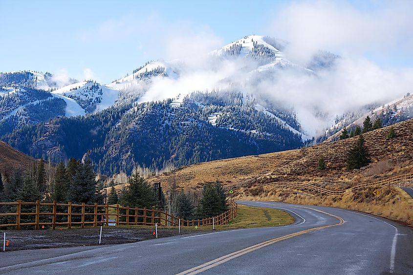  A winding road in Sun Valley, Idaho, with snow-dusted mountains rising in the background, partially covered by low-lying clouds. 