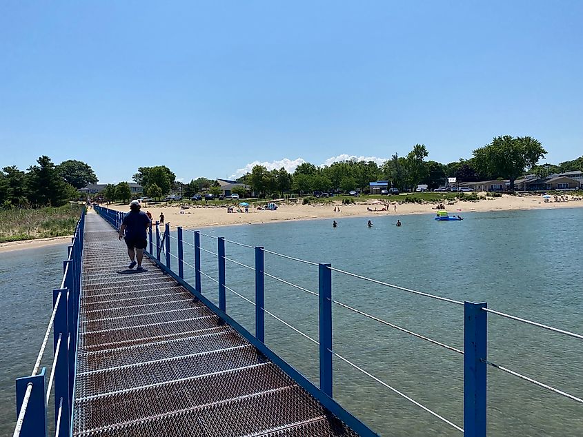 A man walks up a pier toward a sandy beach on a sunny day.