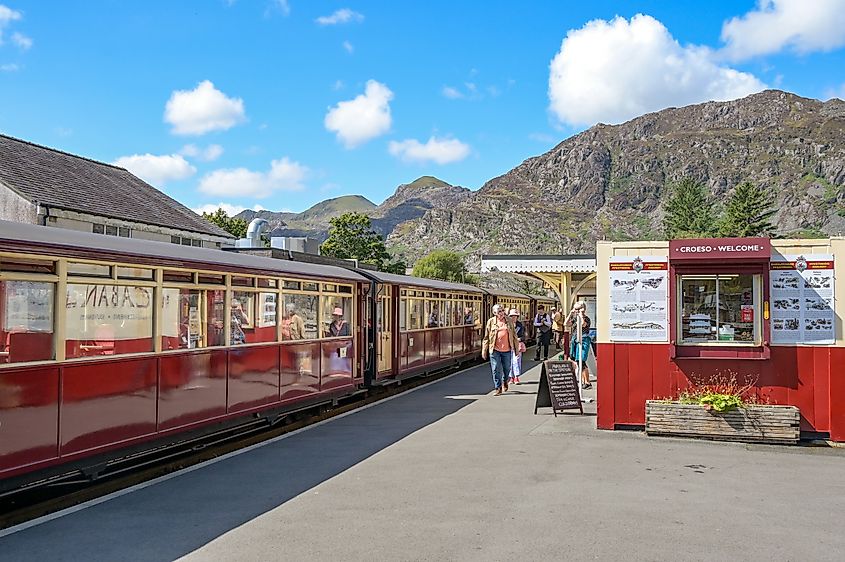 People arriving on a train on the Ffestiniog narrow-gauge railway in Blaenau Ffestiniog. On the left is a ticket kiosk and tourist information office with a welcome sign in English and Welsh.