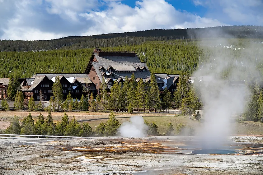 Old Faithful Inn with geysers and steam in foreground.