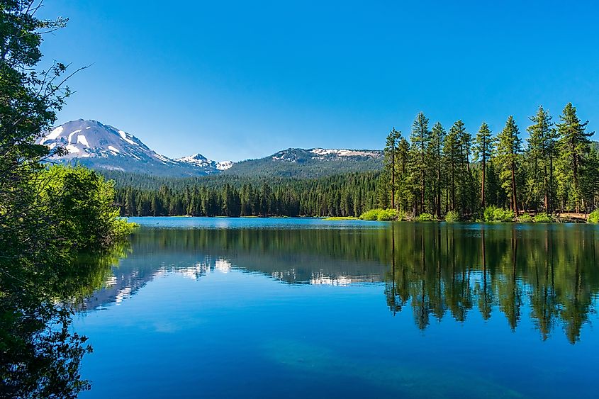 Lassen Peak reflects in beautiful Manzanita Lake in Lassen Volcanic National Park with blue sky.
