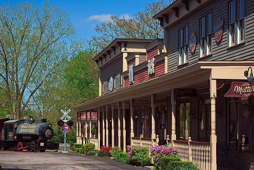 Editorial Photo Credit: Kenneth Sponsler via Shutterstock. Olmsted Falls, OH, USA - April 29, 2024: Old shops with a covered walkway and a vintage steam locomotive with railroad crossbuck are part of the historic district of this Cleveland suburb.