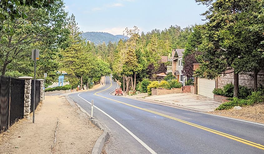 Winding two lane road into Crestline California with green trees lining both sides and a blue sky above