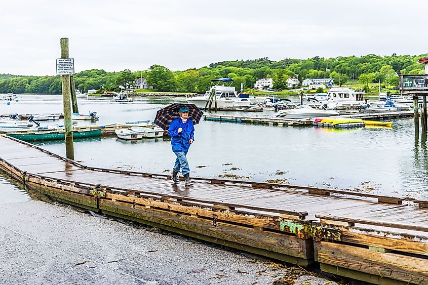Woman with umbrella walking on marina harbor pier in Damariscotta, Maine
