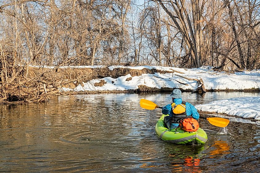 A senior male paddler paddling an inflatable whitewater kayak in the Poudre River during early spring. 