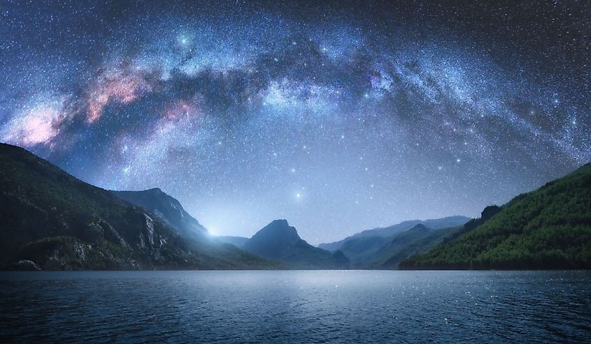 Arched Milky Way over the beautiful mountains and blue sea at night in summer.