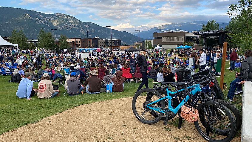 A large crowd gathers before an outdoor stage for a concert in the mountains.