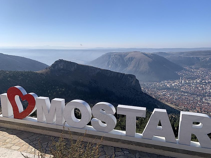 An I Love Mostar tourist sign perched high on a mountain overlooking the valley below. 