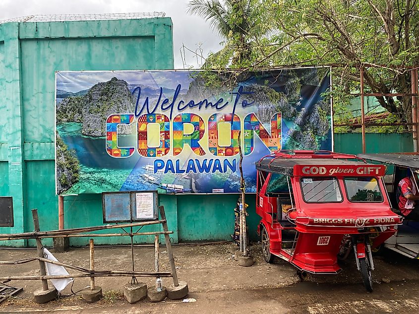 A red tuk tuk parked in front of a colorful tourist sign advertising the Filipino island town of Coron.