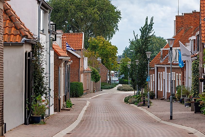 Domburg, Netherlands - August 21, 2025: Picturesque street with brick houses and Dutch flags in the center of Domburg. Via Shutterstock / Pyrrha.studio