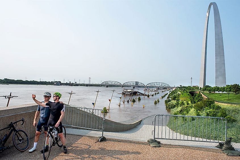 Two men on a bicycle taking selfie in front of the Gateway Arch along a flooded Mississippi River and St. Louis riverfront. Editorial credit: Jon Rehg / Shutterstock.com