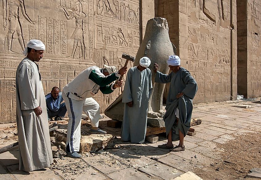EDFU, EGYPT - MARCH 17, 2010 : Workers at the Temple of Horus at Edfu making a new base for one of the carved stone falcons at the pylon entrance. The temple was constructed by Ptolemy III in 237 BC.