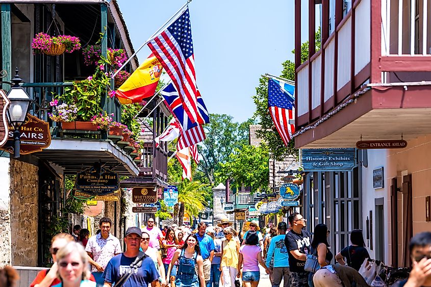 St. Augustine, USA - May 10, 2018: People shopping at Florida city St George Street by stores shops and restaurants in old town city with American and international flags