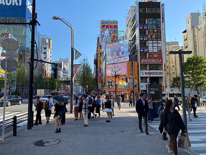 Day time at a shopping district in Tokyo. Anime and other advertisements are splattered on buildings.