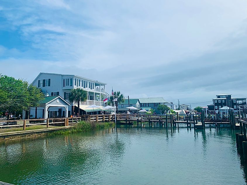 A quiet stretch of waterfront in Swansboro, with docks, low-rise buildings, and reflections on calm water under a cloudy sky.
