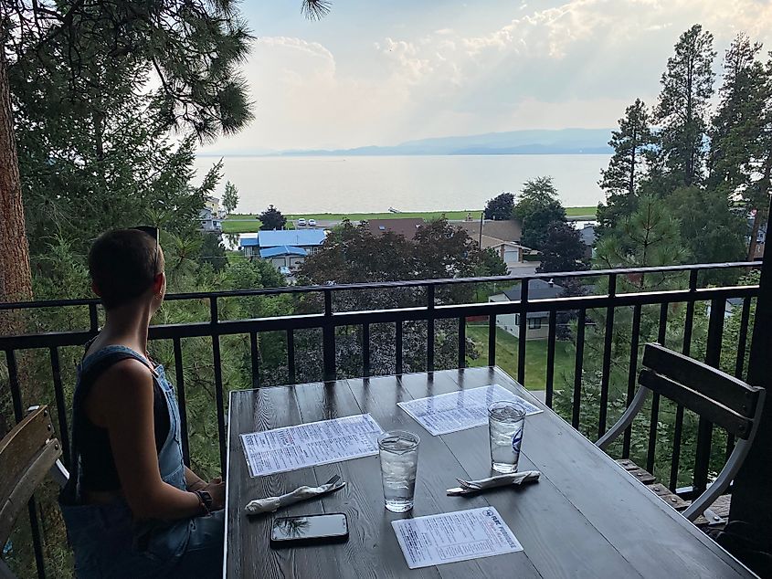 A woman sits at a raised restaurant patio overlooking a the massive Flathead Lake.