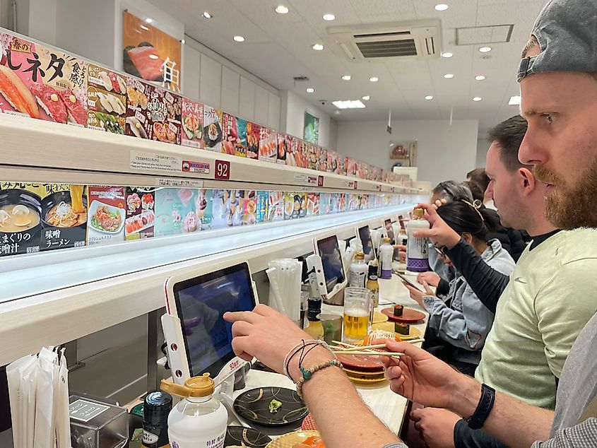 A man fiddles with his ipad at an automated conveyor belt sushi restaurant