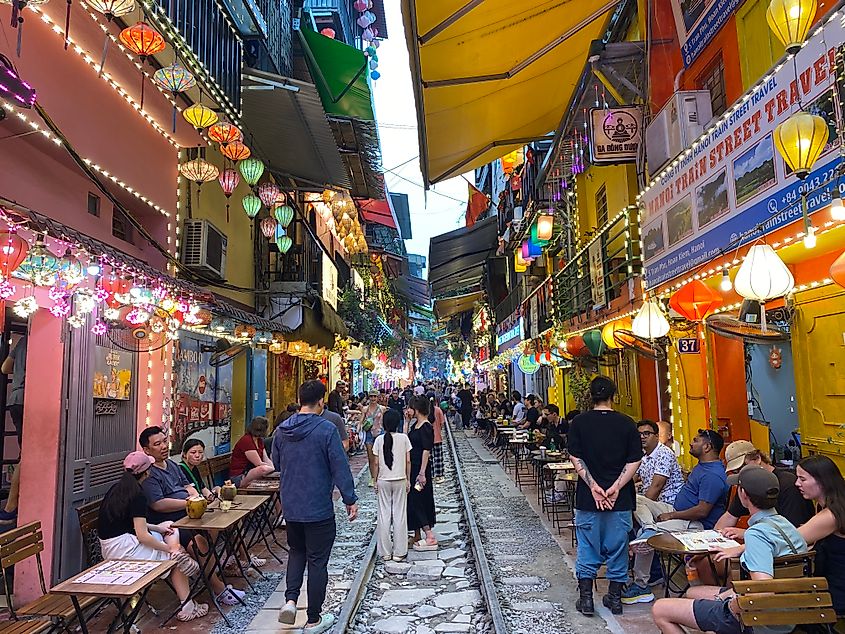 Lots of people walking along an old train track and lining the track-facing cafe seats in anticipation of the next locomotive. A typical scene on Train Street in Hanoi, Vietnam.