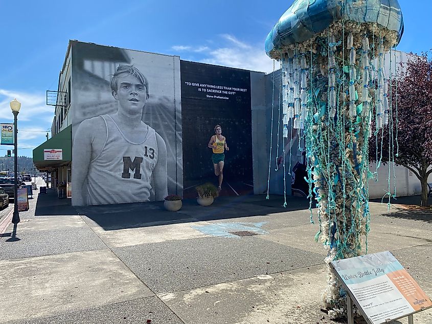 A creative jellyfish statue made of recycled plastic backdropped by a mural of American track star, Steve Prefontaine.