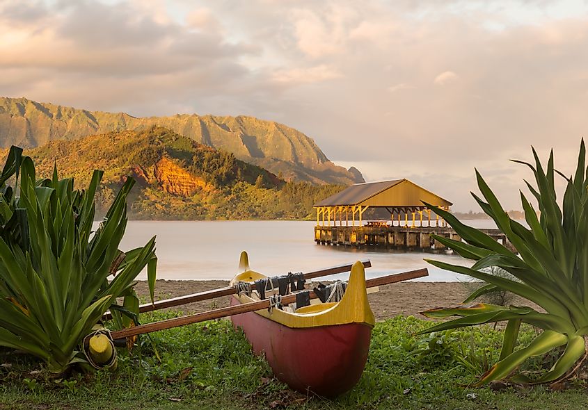 Red and yellow hawaiian canoe with outrigger on the beach at Hanalei pier 