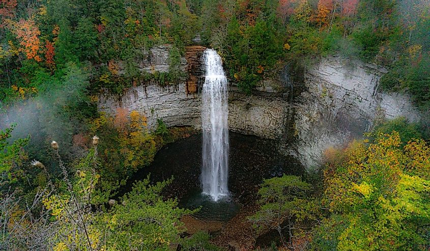 Photo of Falls Creek Falls in an autumn morning mist. Fall colors surround a ribbon of water falling from a rock cliff into a dark pool below. Taken at Falls Creek Falls State Park in Tennessee.