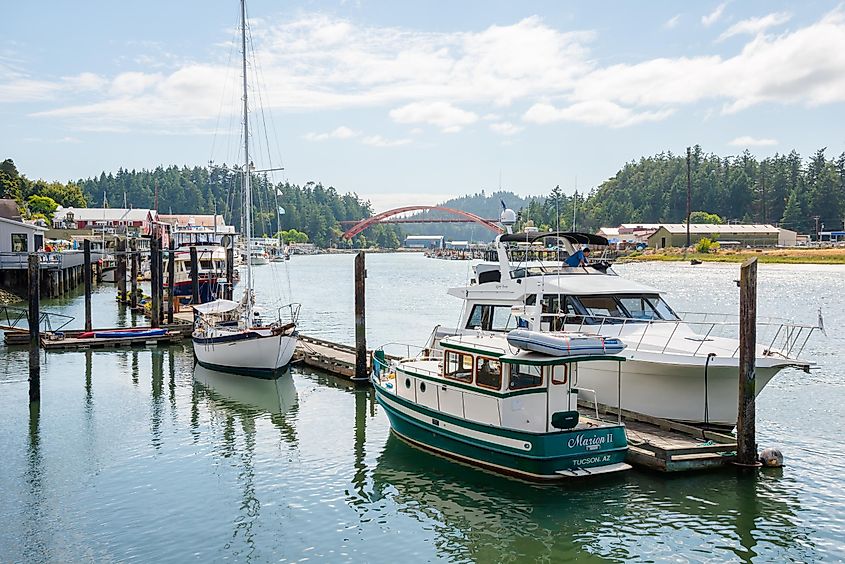 Swinomish Channel with pleasure craft moored at pier along historic waterfront and iconic Rainbow Bridge in popular tourist town of La Conner, Washington.