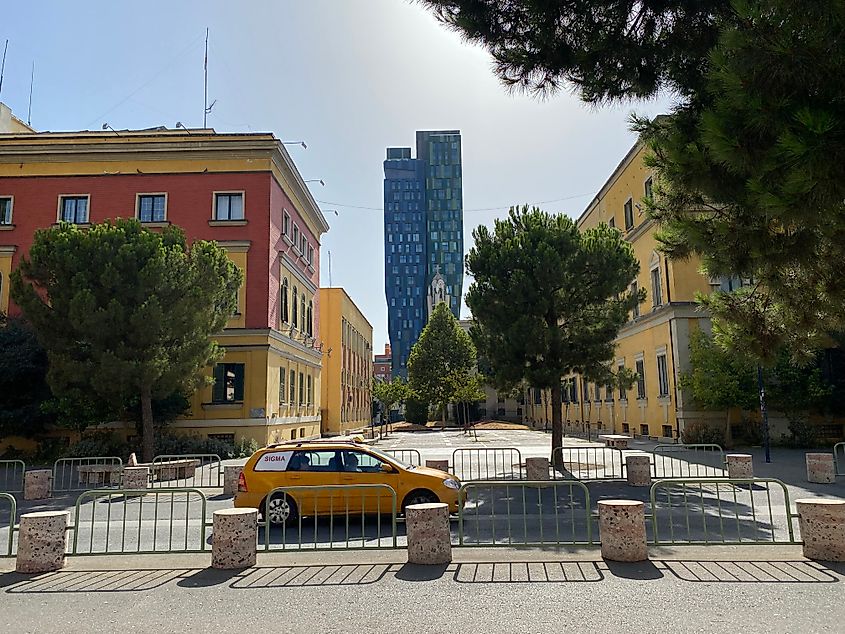 A yellow cab passes colorful buildings and a pair of glass skyscrapers.