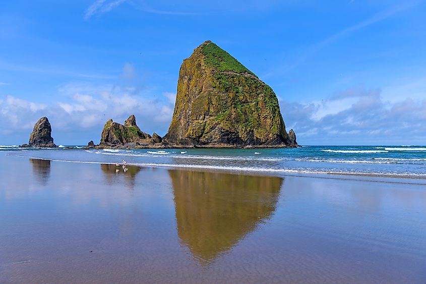 Haystack Rock - A sunny Spring morning view of the famous Haystack Rock reflecting on smooth sandy Cannon Beach. Oregon, USA.