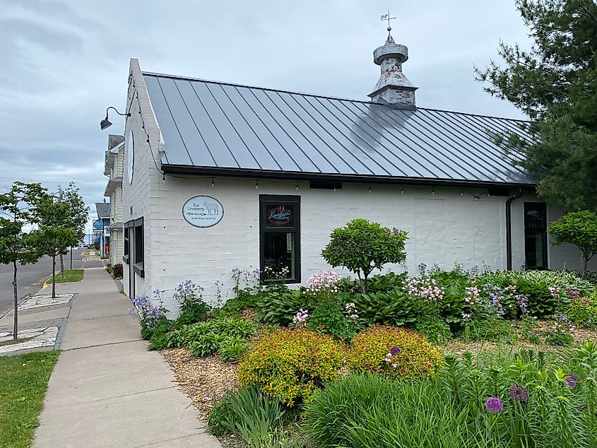 A white bricked shop next to a garden of dense grasses and spring flowers.  