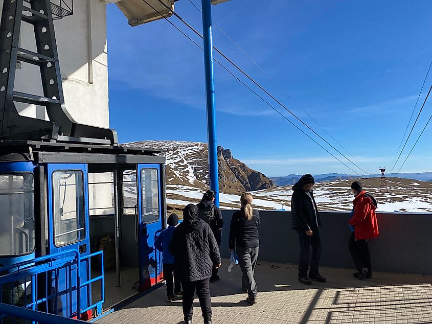 A small group stands outside of a blue cable car at its snowy mountaintop station