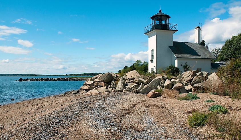 Bristol Ferry lighthouse is surrounded with large boulders to protect the keepers when the tides would rise in Narragansett Bay in Rhode Island. Beach area is covered with open sea shells at low tide.