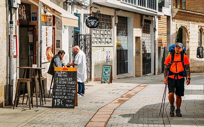 A male backpacker walking past a small tavern advertising a "Pilgrim's Menu"