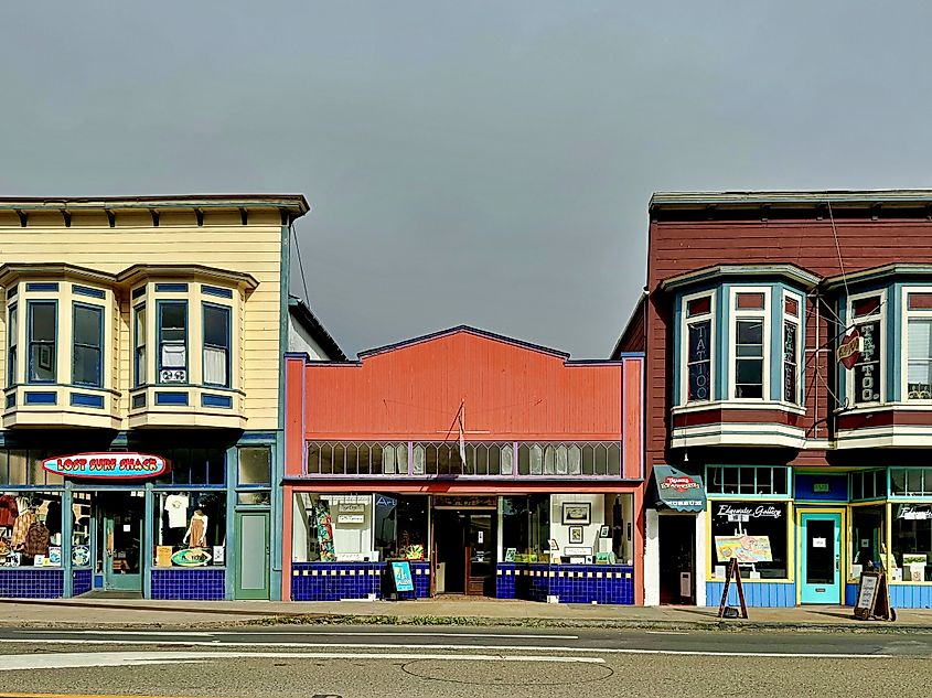 Fort Bragg, California, USA - Sep 15, 2024: Row of historic storefronts in downtown Fort Bragg featuring colorful facades and bay windows, including a surf shop and tattoo parlor. Adele Heidenreich via Shutterstock