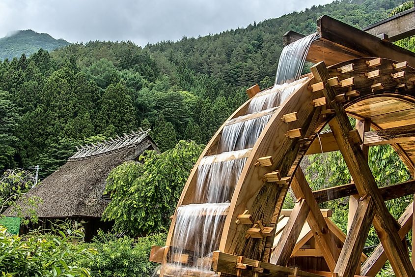 The mill wheel rotates under a stream of water, open air museum at village with traditional thatched roofed houses