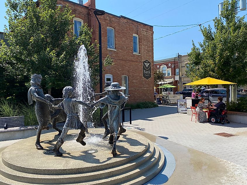 A fountain with a sculpture of a family dancing around it, in an open-air space in a quaint downtown.
