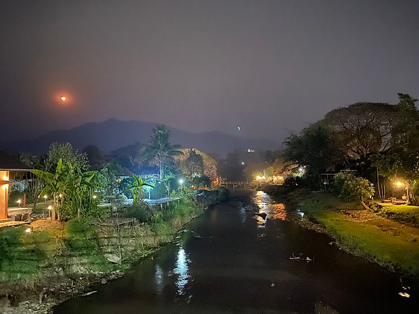 A smoky nightscape with a full moon, mountains, and river.