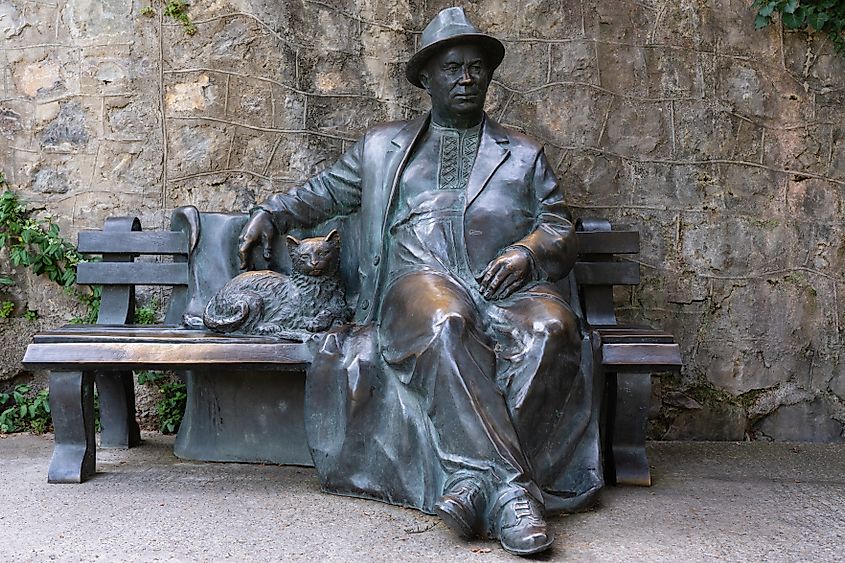 Bronze statue of Nikita Sergeyevich Khrushchev in hat and coat, sitting on bench with cat nearby. Bench is installed near stone wall. Aivazovsky Sanatorium. Partenit, Crimea Editorial credit: Sergey Denisenko / Shutterstock.com