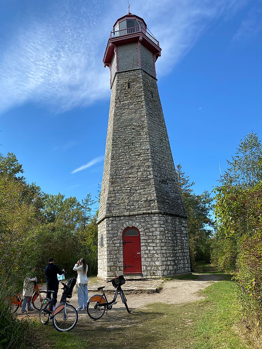 Three people with rental bicycles stop to admire an old stone lighthouse in the woods.