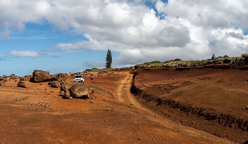 A white Jeep parked at Garden of the Gods on Lanai, Hawaii, next to the Polihua Trail, a volcanic red dirt road